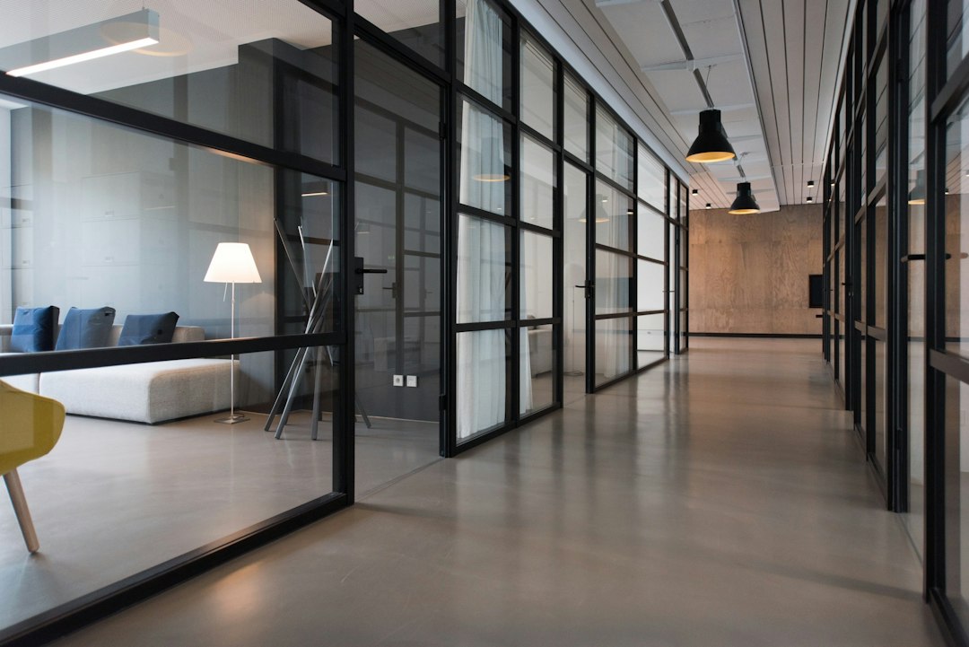 Glass-walled office corridor leading from one workspace to another, natural light